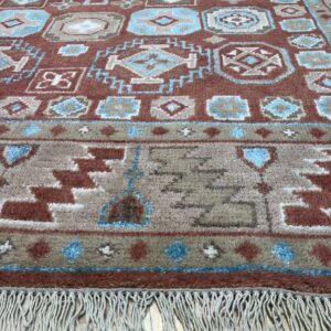 Rust and blue geometric high-pile rug detail with fringe lying on light wood flooring.