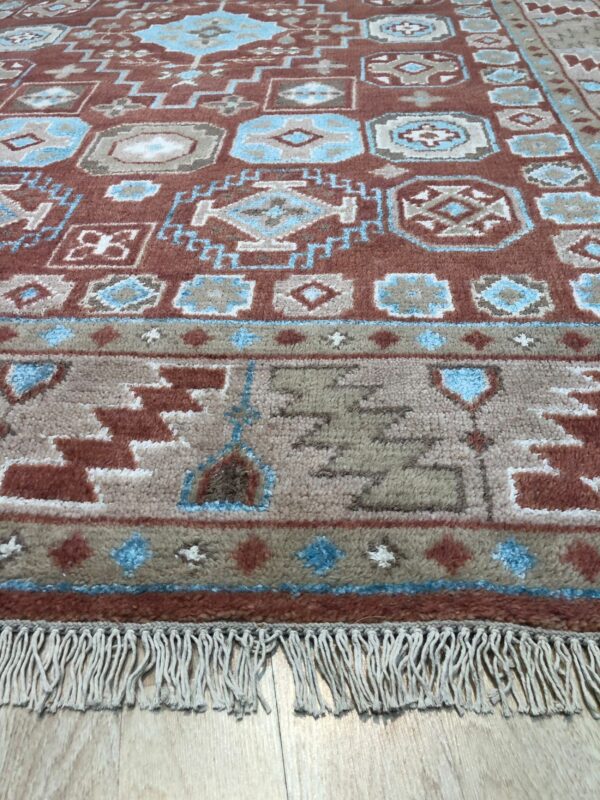 Rust and blue geometric high-pile rug detail with fringe lying on light wood flooring.