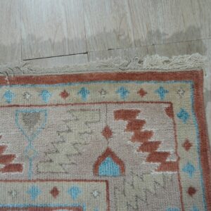 Geometric rug fringe and border in beige, rust, and blue on pale wood plank flooring.