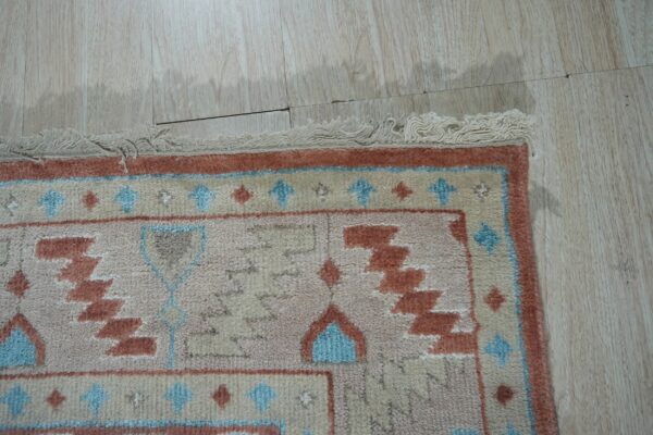 Geometric rug fringe and border in beige, rust, and blue on pale wood plank flooring.