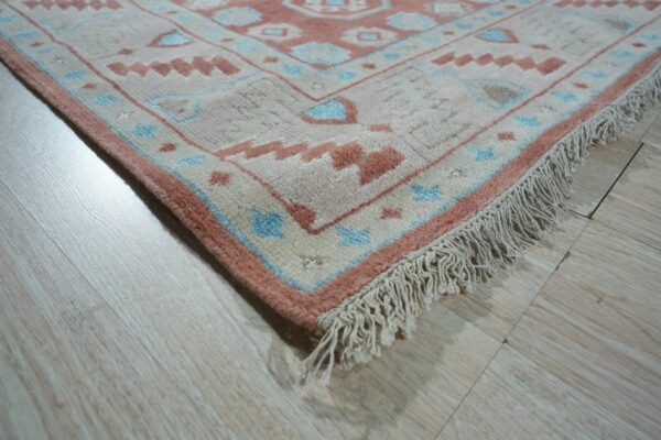 High-pile rug corner in pale pink, blue, and cream tribal patterns with fringe on light wood flooring.