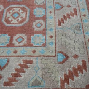 Textured pile rug detail showing rust, beige, and blue tribal geometric patterns and fringe on light flooring.