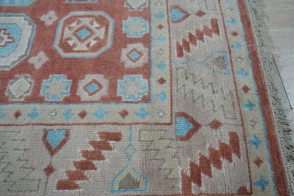Textured pile rug detail showing rust, beige, and blue tribal geometric patterns and fringe on light flooring.