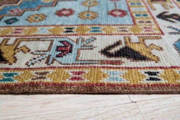 Low-pile rug with geometric patterns in blue, gold, cream, and red resting on light wood flooring.