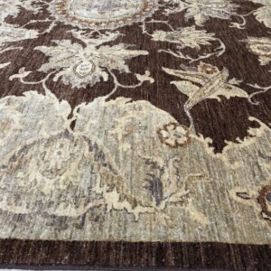 Dark brown rug with a contrasted, distressed beige and taupe floral medallion pattern on pale flooring.