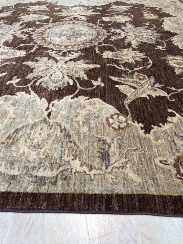 Dark brown rug with a contrasted, distressed beige and taupe floral medallion pattern on pale flooring.