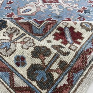 Close-up of a blue tribal rug with red, white, and pink geometric patterns and chunky, textured pile.