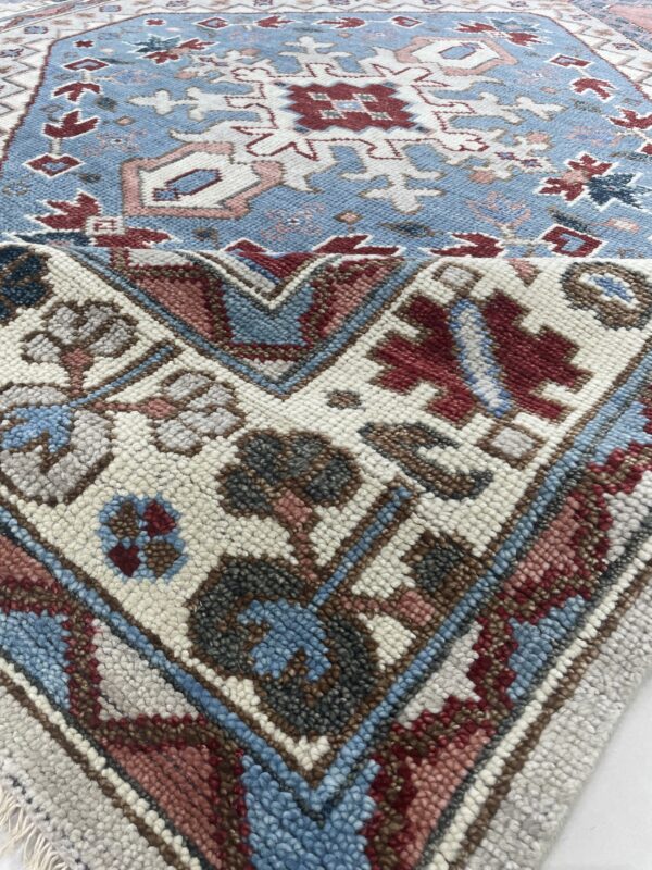 Close-up of a blue tribal rug with red, white, and pink geometric patterns and chunky, textured pile.
