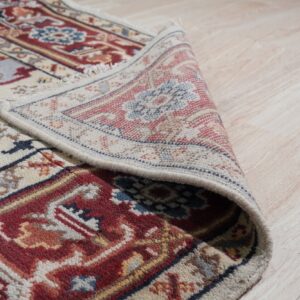 The edge of a red, blue, and cream patterned rug is rolled on light blonde wood flooring.