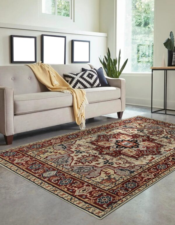 Traditional red, cream, and blue patterned rug displayed under a beige sofa on a modern concrete floor.