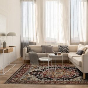 Ornate red, black, and cream area rug beneath white tables in a sunlit living room with a beige couch.