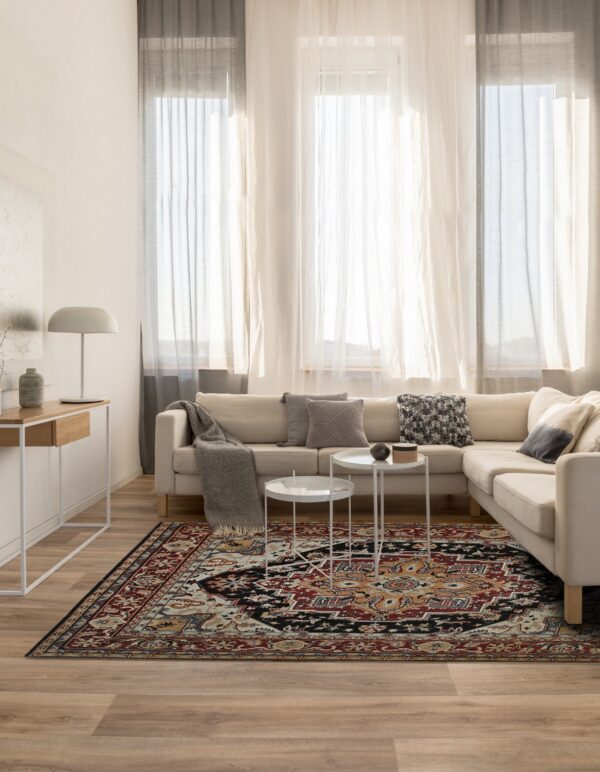 Ornate red, black, and cream area rug beneath white tables in a sunlit living room with a beige couch.