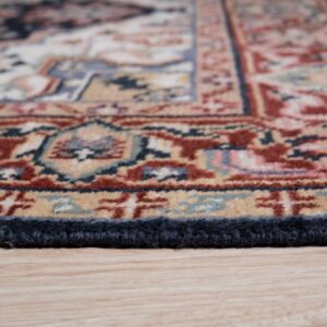 Close-up showing the navy-bound edge of a patterned rug in red, blue, and tan resting on wood floor.