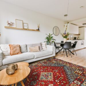 Geometric red and teal area rug anchors a living room near a dining area and white kitchen.