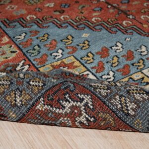 Close-up of a blue and terracotta geometric rug, with the backing folded over light wood planks.