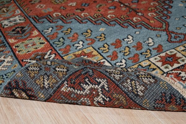 Close-up of a blue and terracotta geometric rug, with the backing folded over light wood planks.