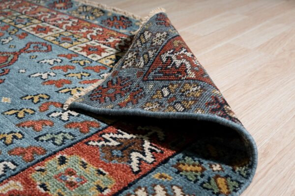 Blue, rust, and cream geometric rug detail, partially rolled up on light wood flooring.