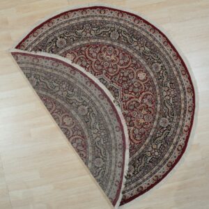 Ornate red and navy floral round rug folded to show the muted reverse side on light wood flooring.
