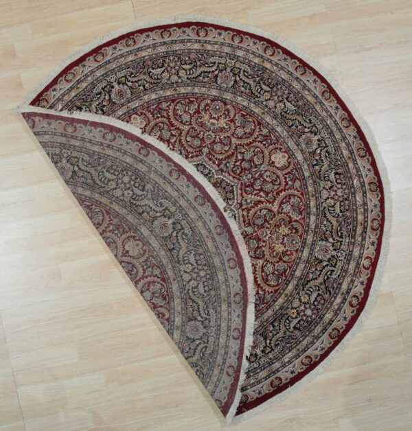 Ornate red and navy floral round rug folded to show the muted reverse side on light wood flooring.
