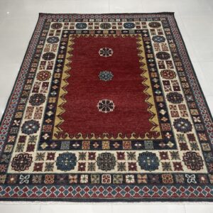 A red traditional rug with navy and cream geometric borders resting on white tile.