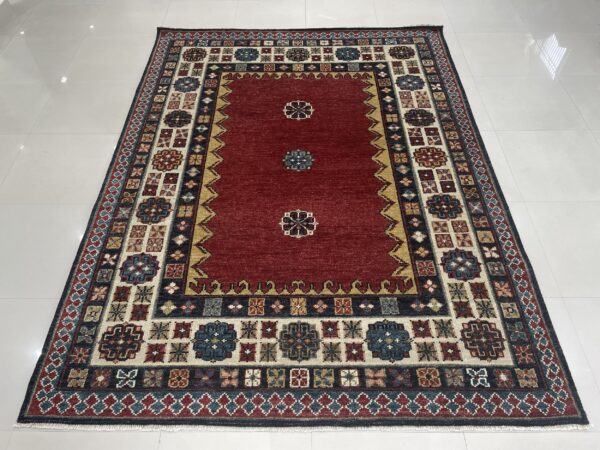 A red traditional rug with navy and cream geometric borders resting on white tile.