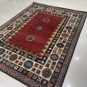 Low-pile rug with a deep red field and detailed geometric borders rests on white tiled flooring.