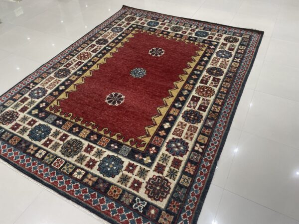 Low-pile rug with a deep red field and detailed geometric borders rests on white tiled flooring.