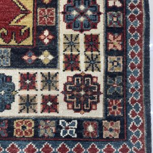 Textured, dense-pile rug displaying geometric patterns and medallions in deep red, navy, cream, and gold colors.