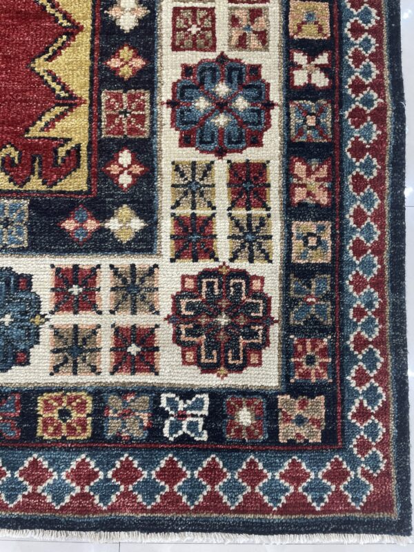 Textured, dense-pile rug displaying geometric patterns and medallions in deep red, navy, cream, and gold colors.