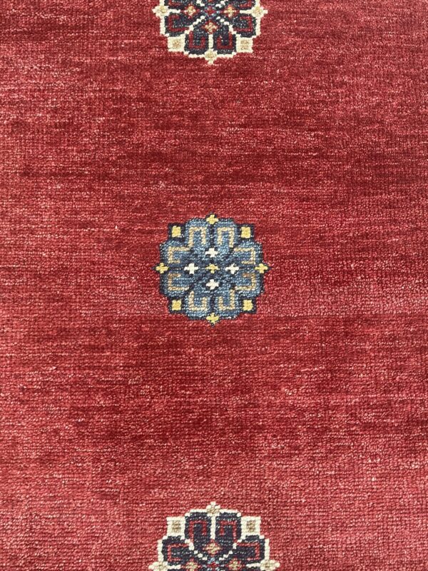 Textured burgundy rug with repeating geometric medallions in blue, cream, and yellow.