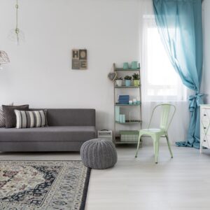 Cream, navy, and burgundy patterned rug under a gray sofa and white side table on light flooring.