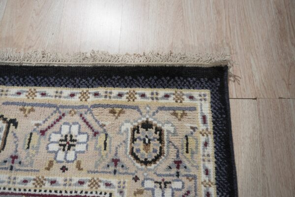 Geometric beige, black, and gray rug with medium pile and fringe detail rests on light wood flooring.