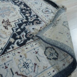 Cream and navy patterned rug corner curled back, revealing the textured backing on light wood flooring.