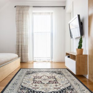 Traditional ivory, navy, and burgundy rug on hardwood floor in a bright room near a bed and wood cabinet.