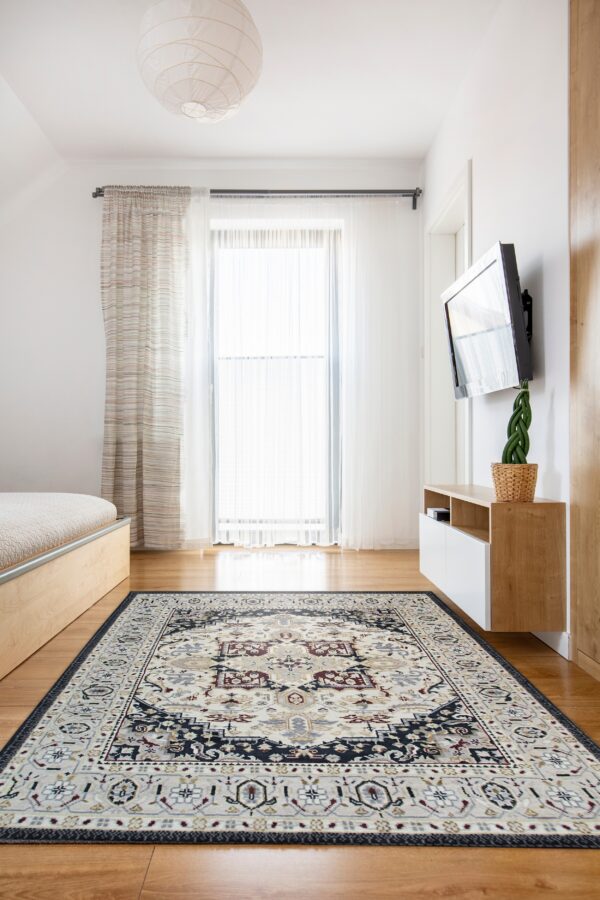 Traditional ivory, navy, and burgundy rug on hardwood floor in a bright room near a bed and wood cabinet.