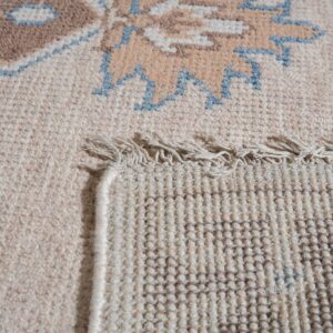 Rug detail showing cream low pile and brown/blue pattern contrasting with the tight woven backing and fringe.