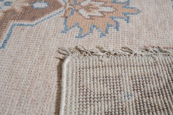 Rug detail showing cream low pile and brown/blue pattern contrasting with the tight woven backing and fringe.