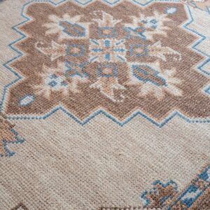 Angled view of a low-pile rug featuring geometric motifs in beige, brown, and light blue.