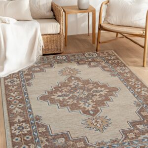 A beige rug with a brown and blue geometric pattern rests between rattan furniture on wood flooring.