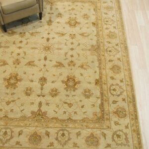Tan and brown traditional rug with an intricate floral pattern displayed on light hardwood, partially under an armchair.