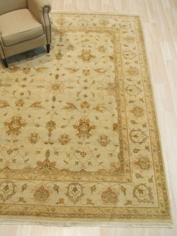 Tan and brown traditional rug with an intricate floral pattern displayed on light hardwood, partially under an armchair.