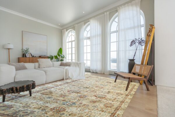Cream and rust traditional rug on wood floors, surrounded by white sofa and large arched windows.