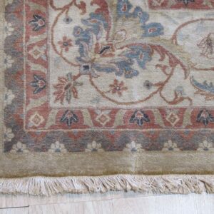 Medium-pile rug detail showing a traditional floral pattern in beige, blue, rust, and gray with fringe on light flooring.