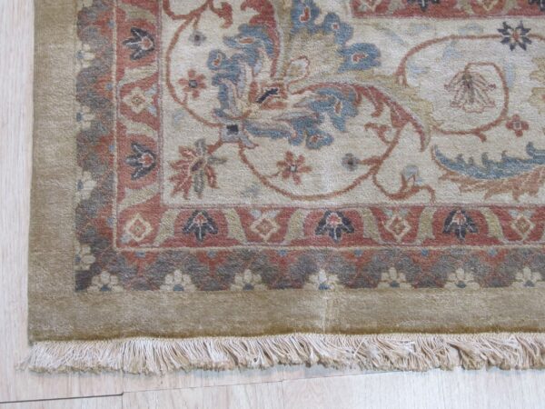 Medium-pile rug detail showing a traditional floral pattern in beige, blue, rust, and gray with fringe on light flooring.