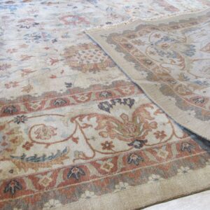 Beige floral rug with red and blue accents, rolled back to show the border on wood flooring.