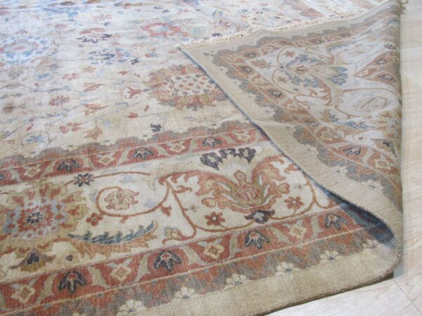 Beige floral rug with red and blue accents, rolled back to show the border on wood flooring.