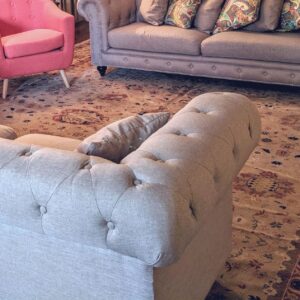 A traditional beige and red patterned rug anchors a living room with two tufted sofas and pink armchairs.