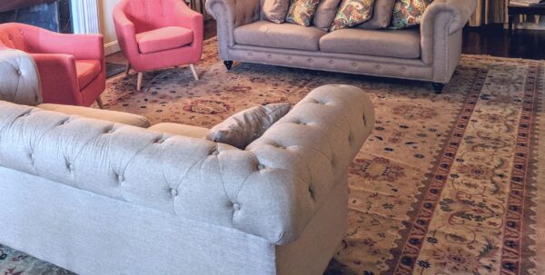 A traditional beige and red patterned rug anchors a living room with two tufted sofas and pink armchairs.