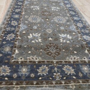 Gray and slate blue runner rug with traditional floral motifs lying on light wood flooring.