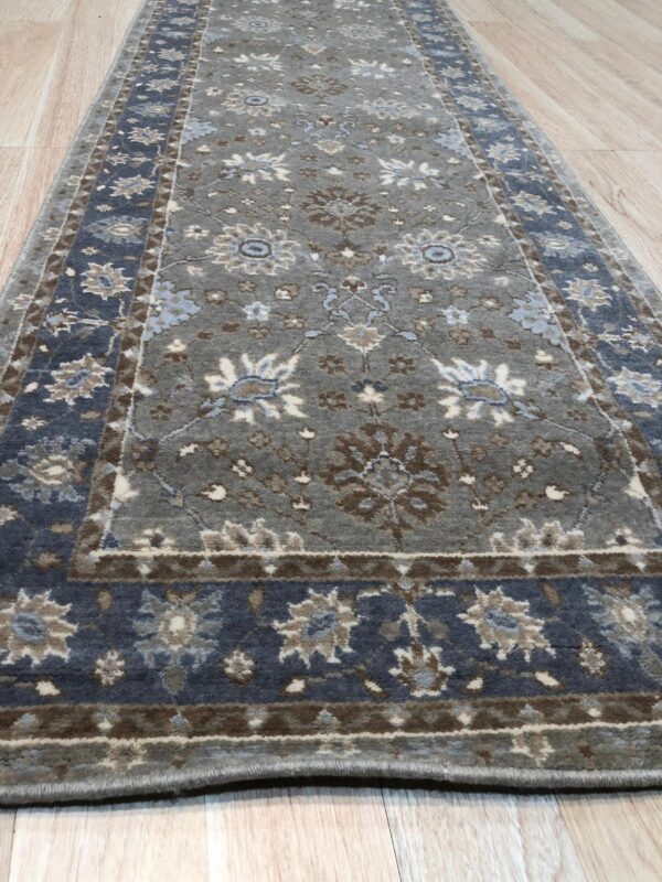 Gray and slate blue runner rug with traditional floral motifs lying on light wood flooring.